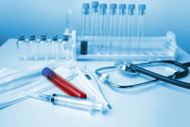 İçinde kan olan tıbbi laboratuvar tüpü, stetoskop, şırınga, koruyucu maskeler, virüsün yayılma tehlikesi ve enfeksiyon konsepti.