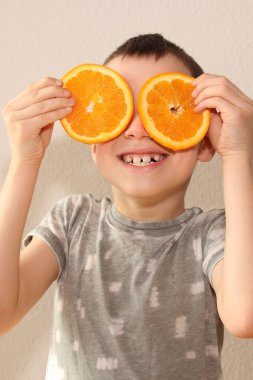 İki portakal dilimi taze, sulu portakallar parlak bir arka planda neşeli bir çocuğu ellerinde tutuyorlar. Sağlıklı beslenme, vitamin, yaşam tarzı...