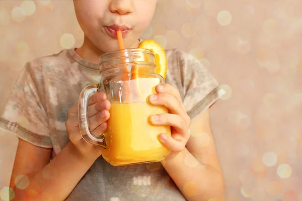 cheerful kid, boy, holds a glass jar in his hand with orange juice from orange or lemon and drinks from a straw, the concept of a healthy diet, vitamins, lifestyle