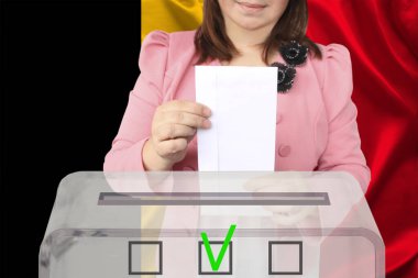 Zeki pembe ceketli kadın seçmen, Belçika bayrağının arka planına karşı saydam bir sandıkta oy kullandı, devlet seçimleri konsepti, referandum
