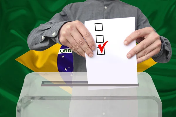 男性の有権者は ブラジルの国旗 州の選挙の概念 国民投票を背景に 透明な投票箱に投票を落とします — ストック写真