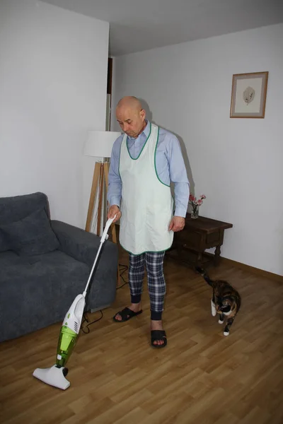 ソファの近くの部屋で家の服やエプロン真空床に55歳のハゲ男 家族の家事の分配の概念 — ストック写真