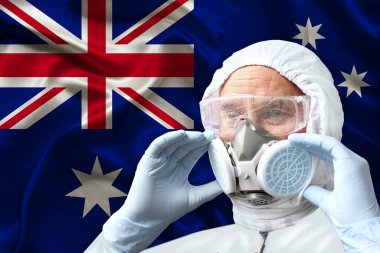 Erkek doktor, koruyucu kıyafetli dezenfektan, solunum cihazı, Avustralya 'nın ipek ulusal bayrağının arka planında duran gözlükler, biyolojik, kimyasal silahlar, koronavirüs, COVID-19 konsepti.