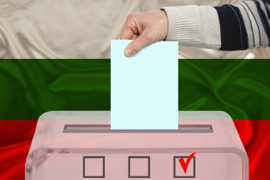 Erkek seçmen, Bulgaristan 'ın ulusal bayrağı, devlet seçimleri ve referandum konseptine karşı şeffaf bir sandık içinde oy kullanıyor