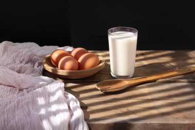 Kahverengi yumurtalar ahşap bir kasede, eski bir kaşık ve bir bardak beyaz süt masanın üzerindeki ışık huzmelerinde, retro konsept