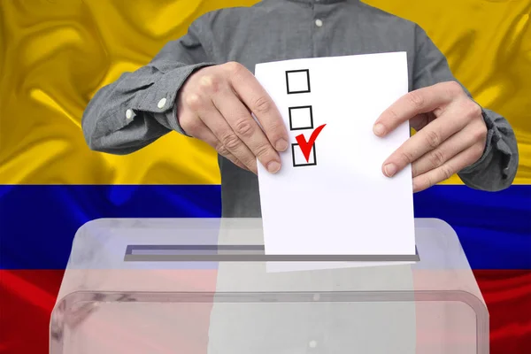 男性の有権者は コロンビアの国旗 州の選挙の概念 国民投票を背景に 透明な投票箱に投票を落とします — ストック写真