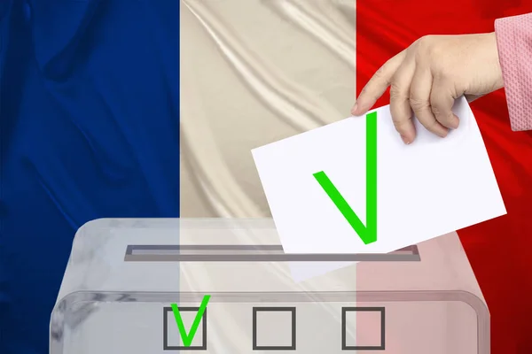 woman voter lowers the ballot in a transparent ballot box against the background of the national flag of france, concept of state elections, referendum