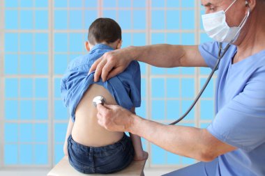 Erkek doktor, steteskoplu çocuk doktoru 7 yaşındaki bir çocuğun akciğerlerini dinliyor, önleyici muayene kavramı, çocukların tedavisi