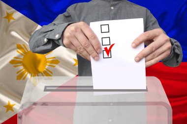 Erkek seçmen, Filipinler ulusal bayrağı, devlet seçimleri konsepti ve referandumun arka planına karşı şeffaf bir sandık içinde oy kullanıyor.