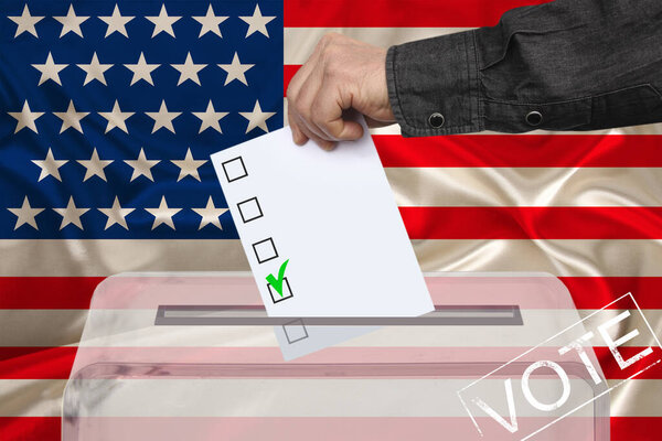 Мужчина-избиратель опускает бюллетень в прозрачную урну для голосования на фоне национального флага Америки, концепции государственных выборов, референдума