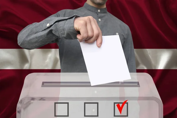 Męski Wyborca Upuszcza Karty Głosowania Przejrzystej Urnie Tle Flagi Łotwy — Zdjęcie stockowe