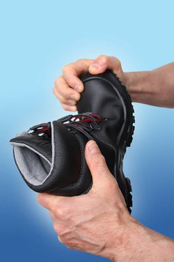 Adam elinde, güçlendirilmiş pelerinli hakiki deriden yapılmış siyah bir çizme tutuyor. Farklı meslekler için özel ayakkabı kavramı.