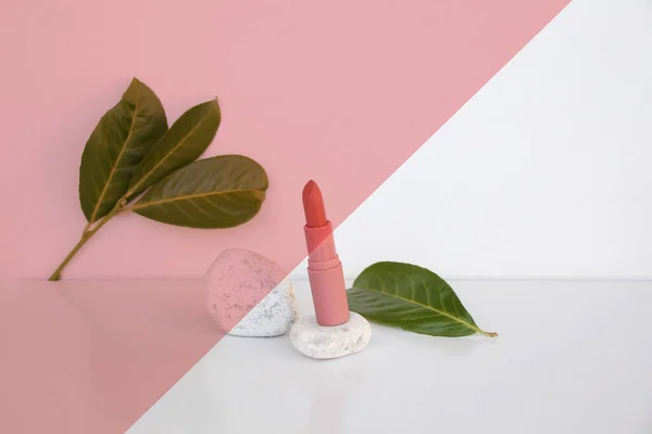 ホワイトピンクの幾何学的背景にピンクの口紅を落とす緑の葉メイクアップ自然装飾化粧品の概念 — ストック写真