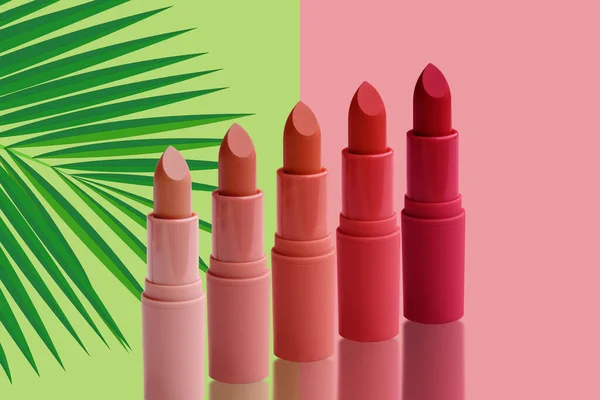 ピンクと赤の口紅のセットは 新鮮な緑 ピンクの幾何学的背景にヤシの葉 自然な化粧の概念 — ストック写真