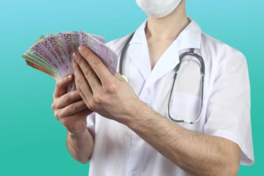 Koruyucu maskeli erkek doktor elinde steteskopla Avro Birliği banknotları, sağlık sigortası, bütçe, tedavi masrafları, organ bağışı hayranı.