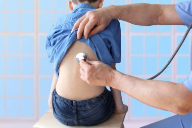 Erkek doktor, steteskoplu çocuk doktoru 7 yaşındaki bir çocuğun akciğerlerini dinliyor, önleyici muayene kavramı, çocukların tedavisi