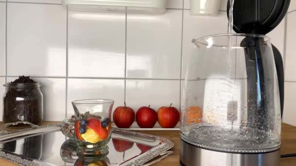 Mann Gießt Wasser Eine Teekanne Eine Glasschale Mit Äpfeln Beeren — Stockvideo