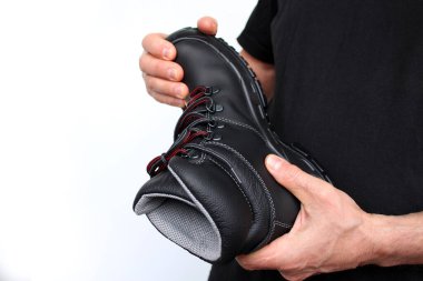 Adam elinde, güçlendirilmiş pelerinli hakiki deriden yapılmış siyah bir çizme tutuyor. Farklı meslekler için özel ayakkabı kavramı.
