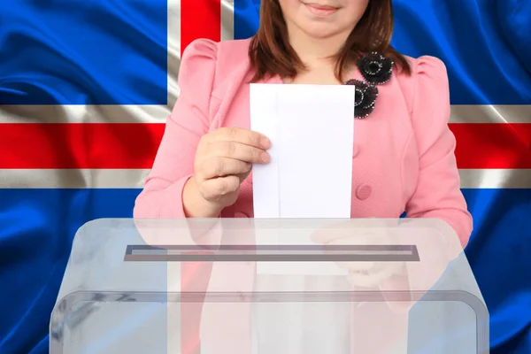 woman voter lowers the ballot in a transparent ballot box against the background of the iceland national flag, concept of state elections, referendum