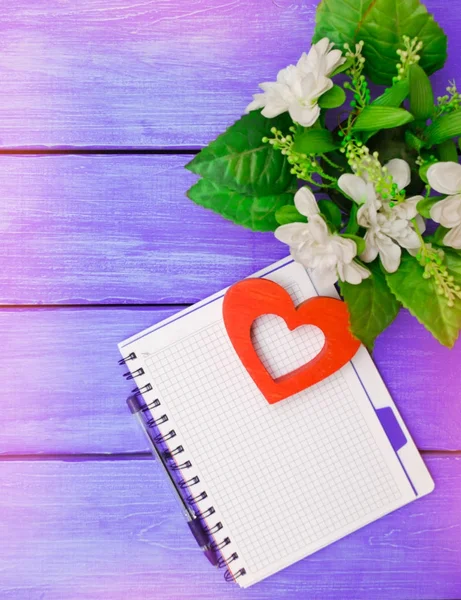 Notebook met pen, bloemen, op een paarse houten achtergrond — Stockfoto