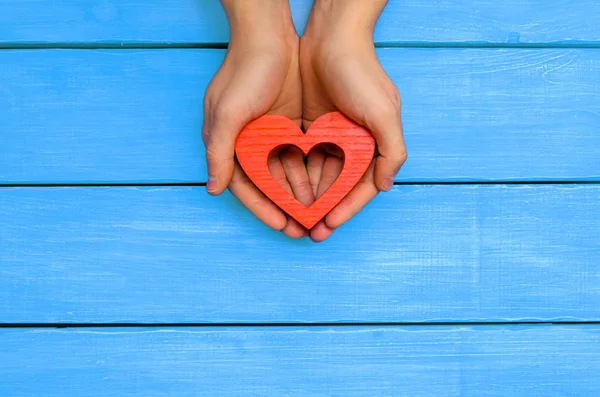 Rode houten hart in handen op een blauwe houten achtergrond — Stockfoto