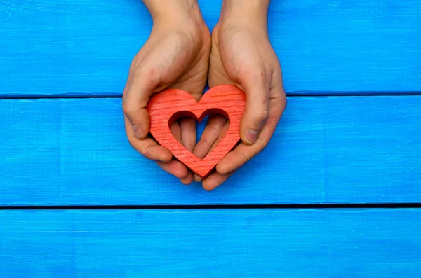 Rode houten hart in handen op een concept van de blauwe houten achtergrond van liefde — Stockfoto