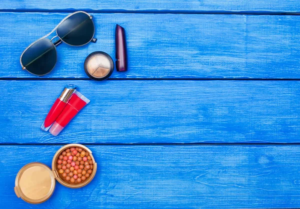 Makeup products on blue wood background, glasses.Flat Lay