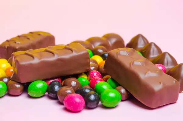 Шоколадные батончики, красочные конфеты, сладости на розовом фоне — стоковое фото