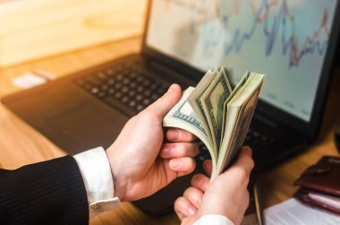 Takım elbiseli bir işadamı bir dizüstü bilgisayar ve mali çizelgeleri elinde bir masada dolar sayar. Bir başarılı bir iş, başarılı satış, tasarruf, yatırım kavramı. Borsası'nda oynarken