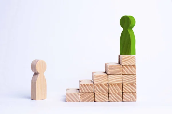 A green man stands at the top of a social or career ladder. Concept of business success. Stairs of people. Use other workers. A wooden figure of a man ascends the stairs to success. — Stock Photo, Image