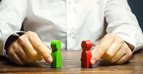 A man holds in his hands the red and green figures of people facing each other. The search for a compromise, mediation in negotiations. Weave intrigue. Conflict resolution, conflict of interest. — Stock Photo, Image