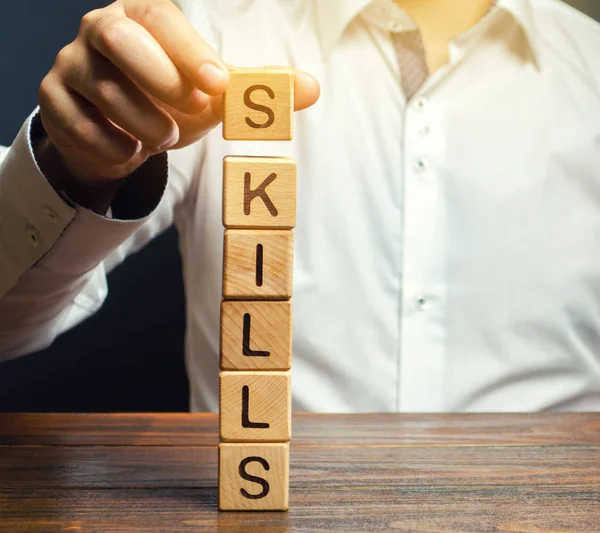 Un hombre pone bloques de madera con la palabra Habilidades. Conocimiento y habilidad. Mejora personal. Concepto educativo. Entrenamiento. Habilidades de liderazgo. Capacidades humanas — Foto de Stock