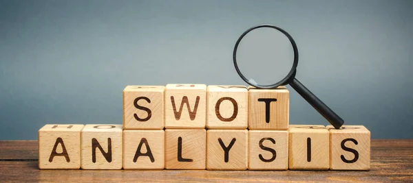 Wooden blocks with the word SWOT analysis and a magnifying glass. The method of strategic business planning. Strengths, weaknesses, opportunities, threats. Business competition or project planning
