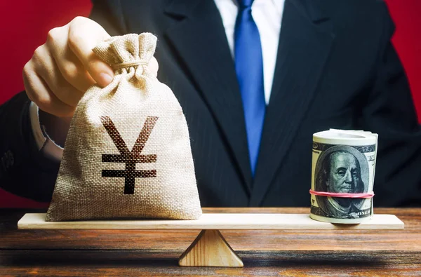 Un homme met un sac d'argent yuan Yen sur les échelles opposées au dollar. Taux de change, comparaison des indicateurs économiques. Éviter l'inflation de l'épargne. Investissements en obligations en devises . — Photo