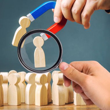 A magnifying glass looks at a magnet pulling wooden figures of people from the crowd. Recruiting new workers, headhunters. Formation of a new business team of applicants. Personnel Management. clipart
