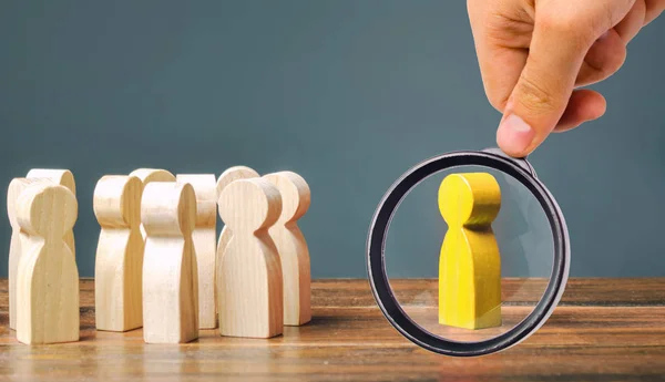 A magnifying glass looks at a yellow figurine of a man stands aside from the crowd of people. Asociality, sociopathy. Rejected from society, lonely. Development of leadership and social qualities. — Stock Photo, Image
