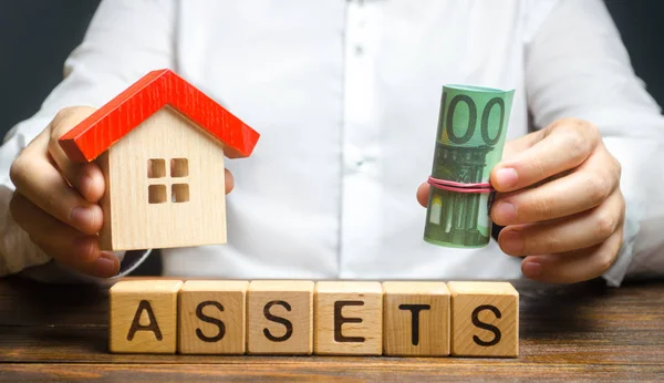 A man holds a house and a bundle roll of Euro over the word Assets. Declaration income and taxation, audit of ownership of real estate and cash. Reliable investment. Property tax — Stock Photo, Image