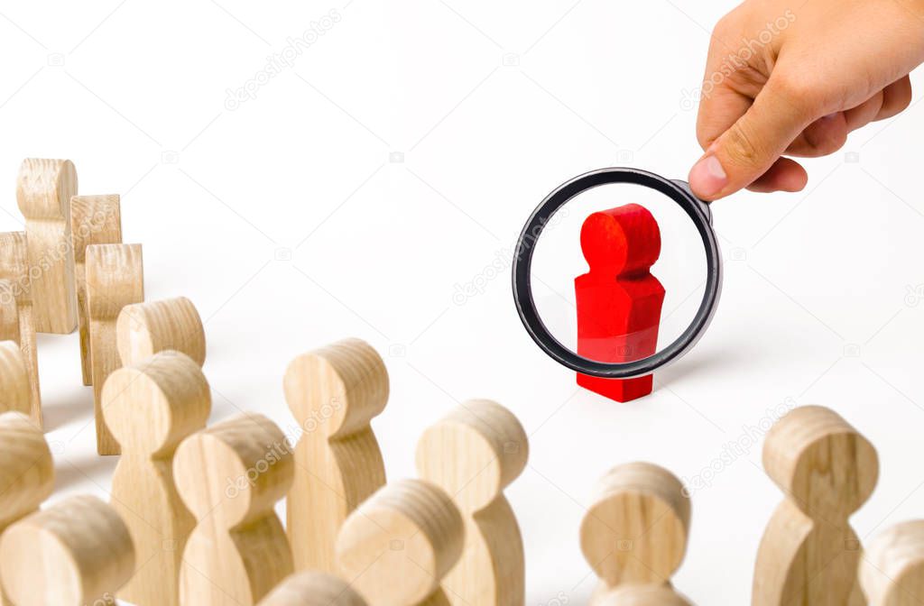 A magnifying glass looks at a red figurine of a man near a crowd. Leader, leadership and initiator of action. work or business organization. team building. Idol and example to follow. Distrust