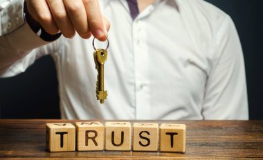 Güven kelimesinin geçtiği tahta bloklar ve anahtarlar bir işadamının elinde. Apartman, araba, mülk ve gayrimenkul. Kredi notu. Kiralık garanti. Güvenilir ortak