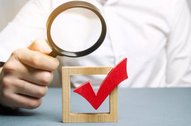 Bir adam kırmızı işaret işaretini büyüteçle inceliyor. Seçim veya referandumun meşruluğunun şeffaflığı değerlendiriliyor. Yasadışı balta, sahtecilik ve ihlaller. Demokrasi.