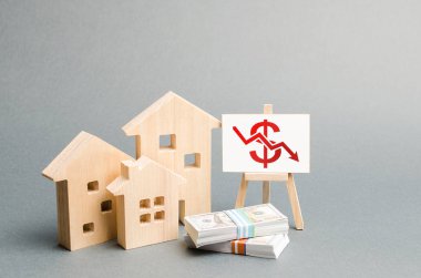 Wooden figures of houses and a poster with a symbol of falling value. concept of real estate value decrease. low liquidity and attractiveness of assets. cheapening the rent or cost of buying a home clipart