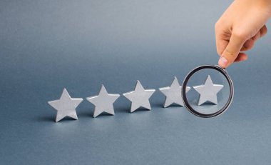 Büyüteç gri arkaplandaki beş yıldıza bakıyor. Derecelendirme ve değerlendirme konsepti. Otelin, restoranın, mobil uygulamanın derecesi. Kaliteli hizmet, alıcı seçimi. Başarı