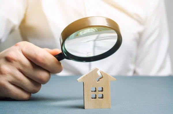 A man with a magnifying glass looks at a house with a crack. Damage assessment home and insurance risks. Estimation of the cost of repair and renovation of old buildings, property value.