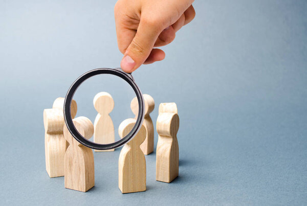 Magnifying glass is looking at people stand in a circle on a gray background. Wooden figures of people. A circle of people. discussion, cooperation, cooperation. teamwork, team spirit. Selective focus