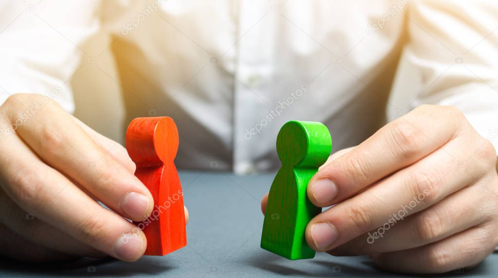 A man holds in his hands the red and green figures of people facing each other. The search for a compromise, mediation in negotiations. Weave intrigue. Conflict resolution, conflict of interest.