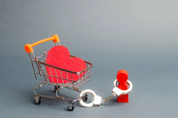 person is handcuffed to a red heart on a supermarket cart. Man is limited in freedom of action. Difficulties in love, non-reciprocal love. Organization of divorce, legal obstacles. Prostitution