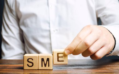 Businessman holds wooden blocks with the word SME. Small and medium-sized enterprises - commercial enterprises that do not exceed certain indicators. clipart