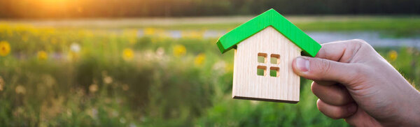 Wooden house in the hands in the sunset background. Real estate concept. Eco friendly home. Symbol of happy family life. Buy a housing outside the city. Search for hotel on vacation. Selective focus