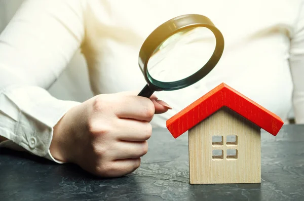 A woman is holding a magnifying glass over a wooden house. Real estate appraiser. Assessment of the condition of the house. Property valuation / appraisal. Search for housing and apartments. — Stock Photo, Image