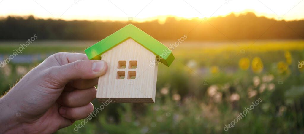 Wooden house in the hands in the sunset background. Real estate concept. Eco friendly home. Symbol of happy family life. Buy a housing outside the city. Search for hotel on vacation. Selective focus